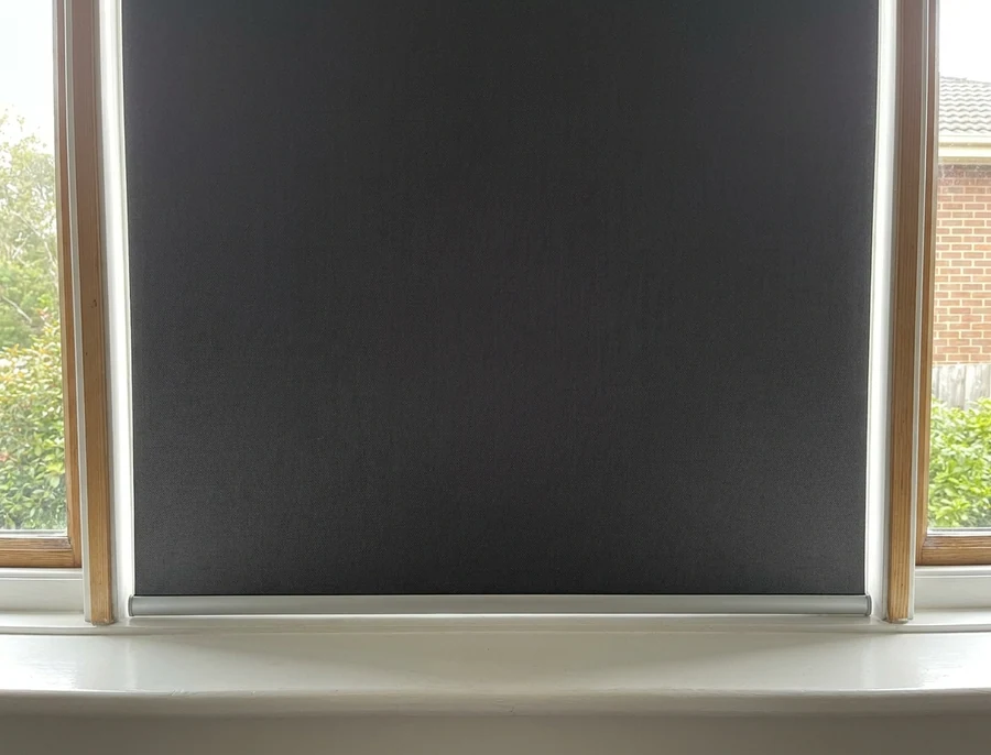 Blockout roller blind fully lowered over a home-office window, straight-on view of the flat fabric panel and its tidy bottom bar